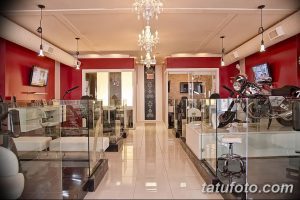 Фото тату-студии с преобладанием красного цвета, стильной мебелью и мотоциклом в качестве декоративного элемента. Подходит для любителей байкерской тематики.