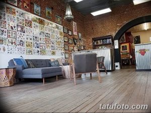 Фото тату-студии с огромной стеной, увешанной эскизами татуировок, мягкой мебелью и уютной атмосферой. Пространство для творчества и вдохновения.