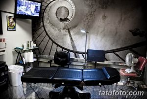 Фото современной тату-студии с винтовой лестницей, удобным креслом для клиента и профессиональным оборудованием. Стильный интерьер и комфортная атмосфера.