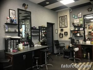 Фото стильной тату-студии с большими зеркалами, примерами рисунков татуировок на стенах и профессиональным оборудованием. Современный дизайн и комфортная атмосфера.