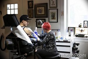 Фото процесса нанесения татуировки: мастер с красными волосами делает татуировку клиенту, используя современное оборудование.