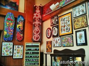 Фото тату-студии с яркими рисунками в рамках, неоновой вывеской 'TATTOO' и разноцветными скетчами на стенах.