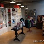 Фото просторного магазина тату-арта и аксессуаров с белыми полками, различными предметами декора и одеждой. Атмосфера творчества и стиля.