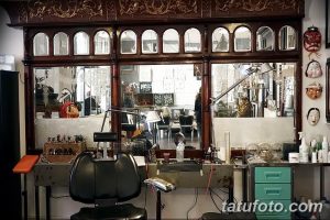 Фото рабочего места мастера тату в тату-салоне с антикварной мебелью, зеркалами и различными декоративными элементами. Атмосфера творчества и мастерства.