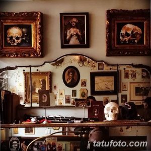 Фото интерьера тату-салона в винтажном стиле с черепами в рамах, портретами и тату-оборудованием. Атмосфера таинственности и творчества.