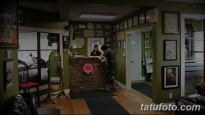 Фото интерьера тату-студии с каменной стойкой ресепшн, множеством эскизов на стенах и удобными креслами для клиентов.