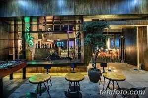 Фото интерьера тату-студии с неоновой вывеской, деревянной мебелью и растениями.