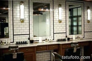 Фото стильной тату-студии с зеркалами, белой плиткой и винтажными светильниками. Видны раковины и кресла для клиентов.