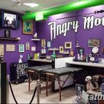 Фото интерьера тату-студии 'Angry Monkey' с фиолетовыми стенами и ярким оформлением. Видны рабочие места мастеров и элементы декора.
