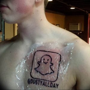 Фото тату с изображением белого призрака Snapchat на груди мужчины, покрытой защитной пленкой. Простой контурный рисунок.