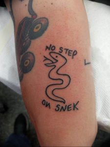 Фото татуировки с изображением змеи и надписью 'No step on snek'. Черно-белый рисунок, минималистичный стиль, юмористическая татуировка.