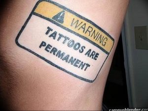 Фото татуировки в виде предупреждающего знака с надписью 'Warning: Tattoos are permanent'. Черно-желтый рисунок, минималистичный стиль, ироничная татуировка.
