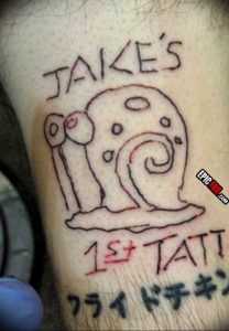 Фото тату: простая, наивная татуировка улитки с надписью "Jake's 1st Tatt". Первая татуировка, выполненная в любительском стиле.
