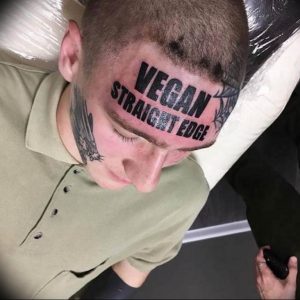 Фото тату: татуировка надписей "VEGAN STRAIGHT EDGE" на лице мужчины. Экстремальный стиль и выражение личных убеждений.