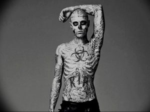 Фотография мужчины с татуировкой, имитирующей скелет и другие мрачные символы на лице и теле. Татуировка выполнена в черно-белой гамме.
