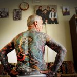 Фотография мужской спины, покрытой большой японской татуировкой с изображением карпа кои, волн и цветов.