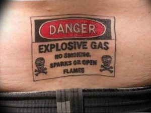 Фото татуировки в виде знака опасности с изображением черепов и надписью "Explosive Gas". Оригинальный и провокационный рисунок.