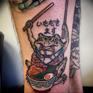Фото тату на руке с изображением лягушки в кимоно, поедающей рамен, и иероглифами.