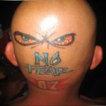 Фото тату на затылке с изображением двух злых глаз и надписью 'NO FEAR' с огненными элементами.