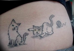 Милая татуировка на боку, изображающая двух котят, играющих с клубком ниток. Черно-белый рисунок с небольшими цветными акцентами.