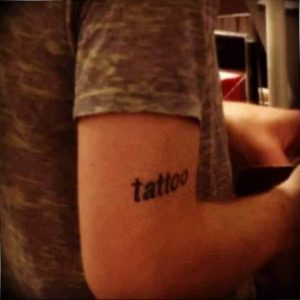 Фото тату на руке с надписью 'tattoo'. Простой шрифт и черные чернила делают рисунок минималистичным и стильным.