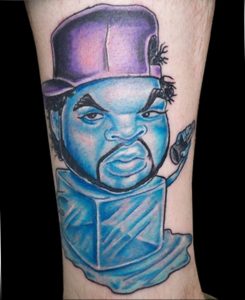Фото тату на руке с реалистичным портретом рэпера Ice Cube в его фирменной шапке и с кубиком льда. Яркие цвета и детализированная проработка.