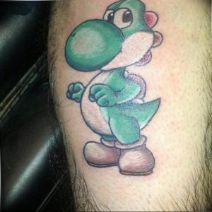 Фото татуировки на руке с изображением зеленого динозавра Йоши из видеоигры Super Mario.