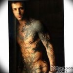 Фотография мужчины с татуировкой дракона, покрывающей его грудь, плечо и руку. Татуировка выполнена в черных тонах и имеет детализированную текстуру.