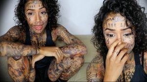 Фото тату: Девушка с экстремальными татуировками на лице, шее, руках и теле. Рисунок татуировки выполнен в различных стилях, включая надписи и геометрические узоры.
