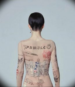 Фото тату на спине девушки. Разнообразные рисунки, надписи и символы, выполненные в минималистичном стиле, покрывают всю спину.