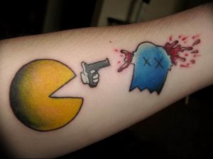 Фото тату: динамичная татуировка с изображением Pac-Man, стреляющего в привидение. Яркие цвета и комичный сюжет.