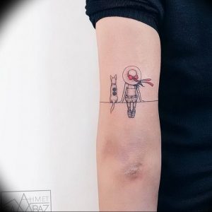 Фото тату: минималистичный рисунок девушки, сидящей рядом с кошкой, выполненный тонкими линиями на локте.