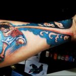 Цветное фото татуировки на руке, изображающей Луффи из аниме One Piece, бегущего вперед на фоне волн. Рисунок выполнен в реалистичном стиле.