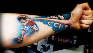 Цветное фото татуировки на руке, изображающей Луффи из аниме One Piece, бегущего вперед на фоне волн. Рисунок выполнен в реалистичном стиле.