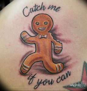 Фото тату: красочный пряничный человечек с надписью 'Catch me if you can' на руке. Веселая и оригинальная татуировка.