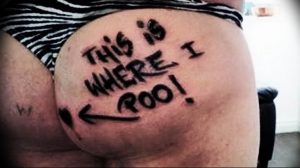 Татуировка на ягодицах с надписью 'THIS IS WHERE I POO!' и стрелкой, указывающей вниз. Необычный и вызывающий рисунок татуировки.