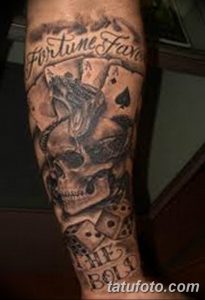 Фото татуировки на руке с изображением черепа, игральных карт, костей и надписи "Fortune Favors". Черно-серые тона и детализированная проработка.