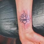 Небольшая, минималистичная татуировка лотоса на запястье, выполненная в черно-белой гамме с использованием тонких линий и точек.