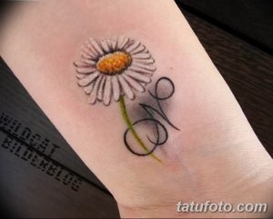 Фотография небольшой татуировки ромашки с символом бесконечности на запястье. Минималистичный дизайн в черном цвете.