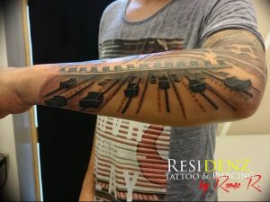 Фото тату: реалистичное изображение клавиш пианино, опоясывающее предплечье. Черно-белая гамма, детализированная прорисовка, музыкальная тематика.