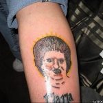 Неудачная татуировка на икре ноги, изображающая портрет женщины с искаженными чертами лица и надписью 'Мама', выполненная в неаккуратной манере.