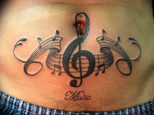 Фото тату на груди с изображением скрипичного ключа, нот и надписи 'Music'. Большой, детализированный рисунок татуировки в черно-белой гамме.