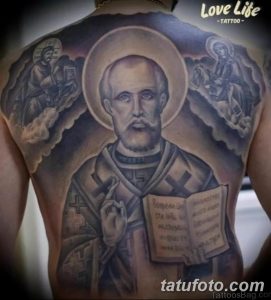 Фото тату Святого на спине, выполненное в реалистичном стиле с использованием черных и серых оттенков. Изображены ангелы и небесные мотивы.