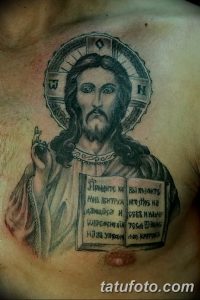 Фото тату иконы Иисуса Христа на плече. Детализированный рисунок с изображением Христа, нимба и древнерусской надписи. Черно-белая татуировка в религиозном стиле.