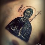 Фото тату Святителя Николая Чудотворца в черно-белом стиле на локте. Детализированный портрет святого с нимбом и книгой.