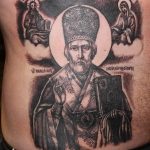 Фото тату Святителя Николая Чудотворца в черно-белом стиле на боку мужчины. Детализированный рисунок с изображением святого, нимба и надписей.