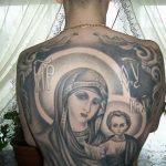 Фото большой татуировки Богоматери с младенцем Иисусом на спине. Черно-серый рисунок татуировки в религиозном стиле с детальной проработкой лиц и одежд.
