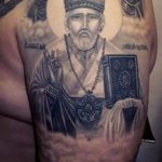 Фото тату священника с книгой на плече. Детализированный черно-серый рисунок с изображением священнослужителя в облачении.