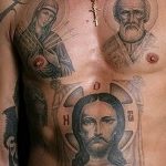 Фото тату Иисуса Христа и святых на груди мужчины. Черно-серый рисунок с изображением ликов святых и креста.