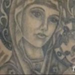 Фото тату Девы Марии с младенцем Иисусом на руке, выполненное в черно-серых тонах с добавлением эффекта свечения. Детализированный рисунок татуировки.
